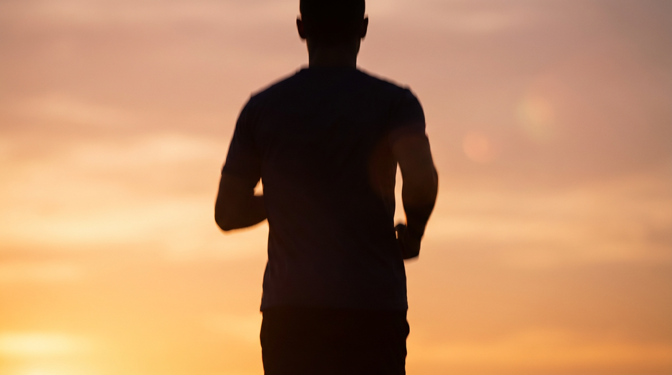 A runner photographed in silhouette from behind at dawn, against a warm gold-and-peach sunrise sky — the emotional shift that shows up by week two.